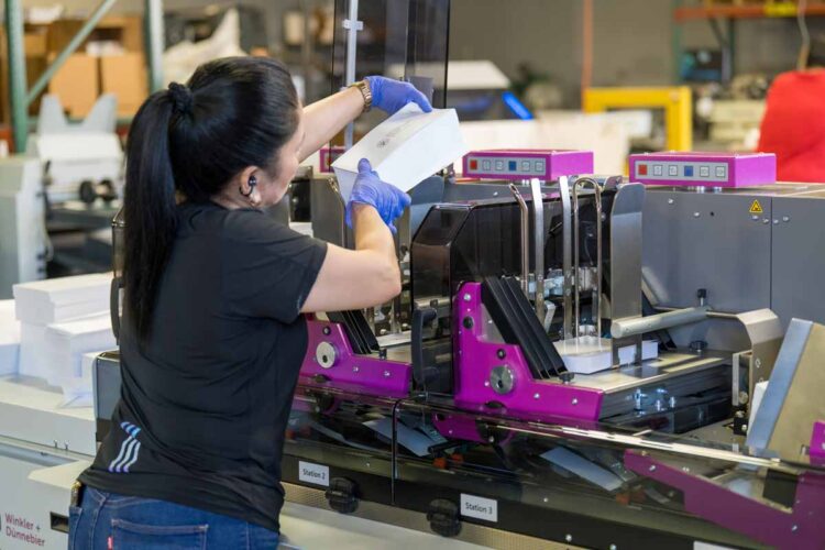 Union worker at Bacchus Press loads mailers in custom machine for processing